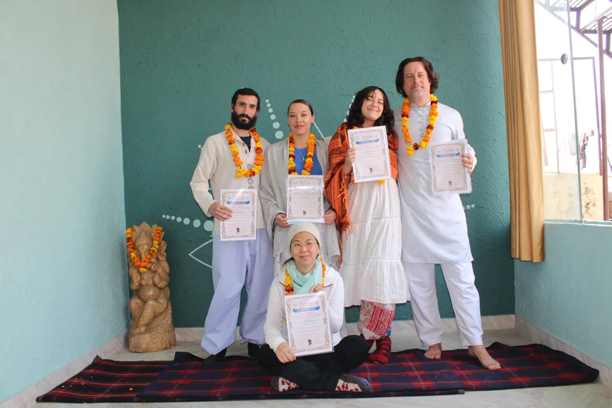 Graduating yoga teacher training students holding their certificates and wearing marigold garlands
