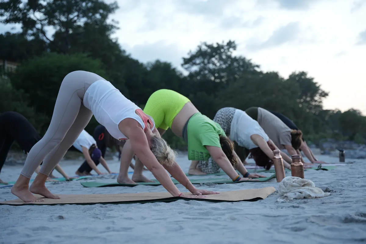 Ashtanga yoga students holding downward facing dog on the Ganges riverbank in Rishikesh