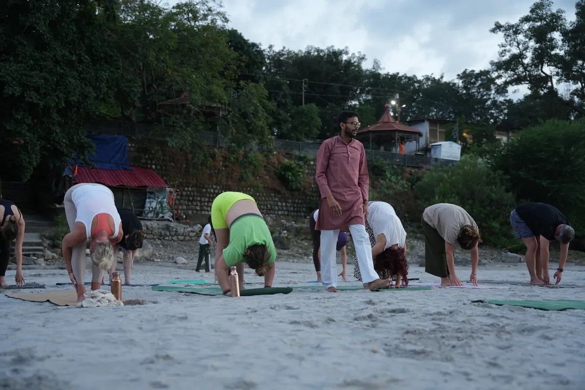 Teacher guiding students through a forward fold during Ashtanga training in Rishikesh