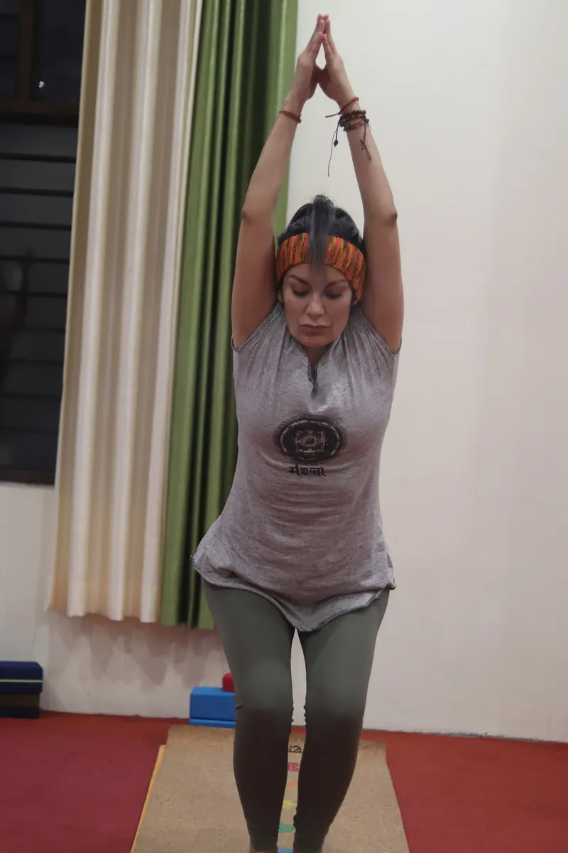 Kundalini yoga student standing with hands overhead in prayer position during class in Rishikesh