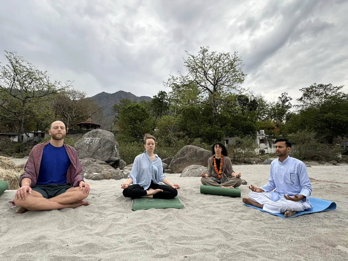 Meditation teacher training students seated cross legged on mats beside the river in Rishikesh
