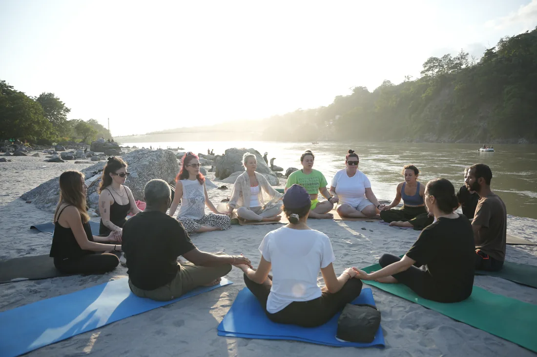 Guests sitting together on the Ganga riverbank at sunrise in Rishikesh
