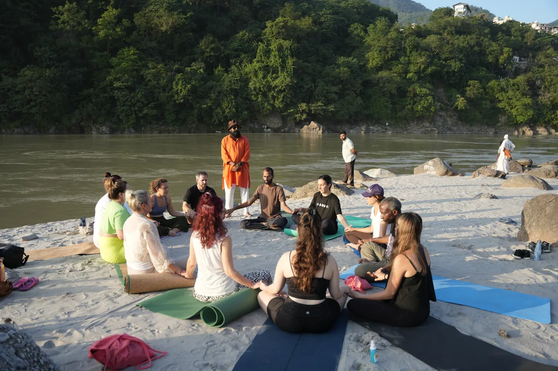 Guests meditating in a circle on the Ganges riverbank at Sri Yoga Ashram, Rishikesh