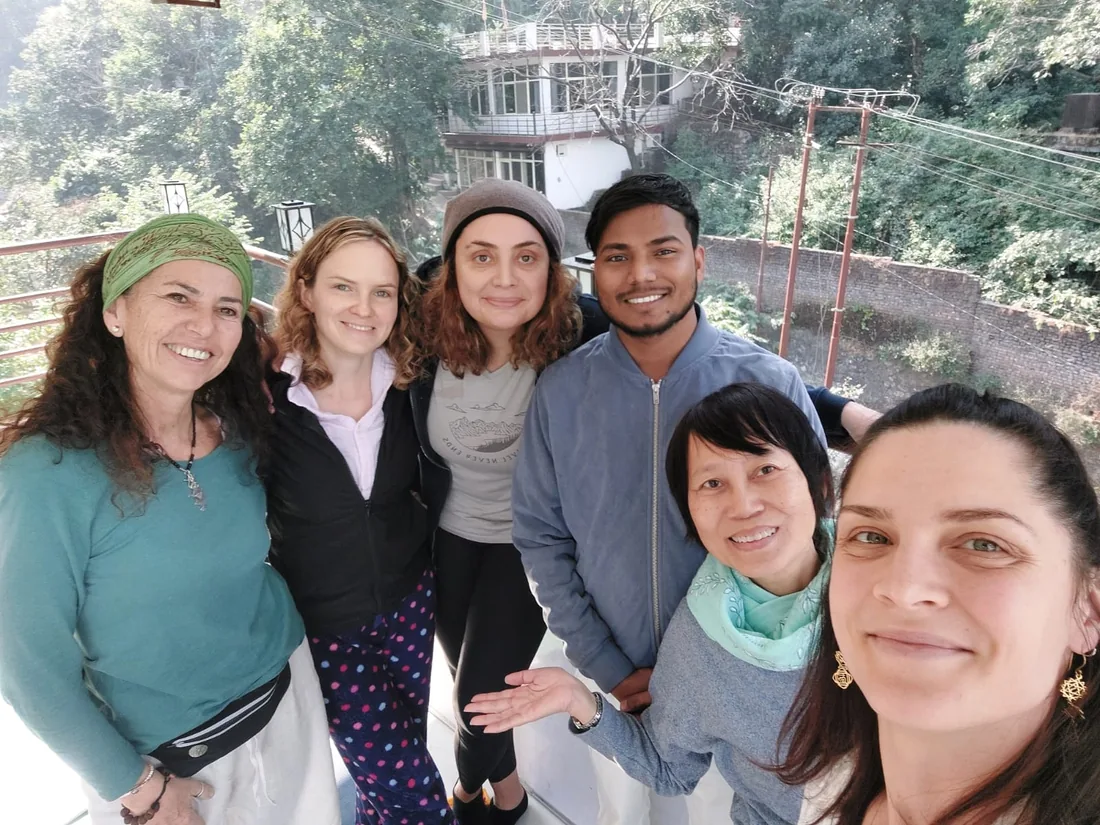 Yoga teacher training students smile together on an ashram balcony above the Rishikesh forest