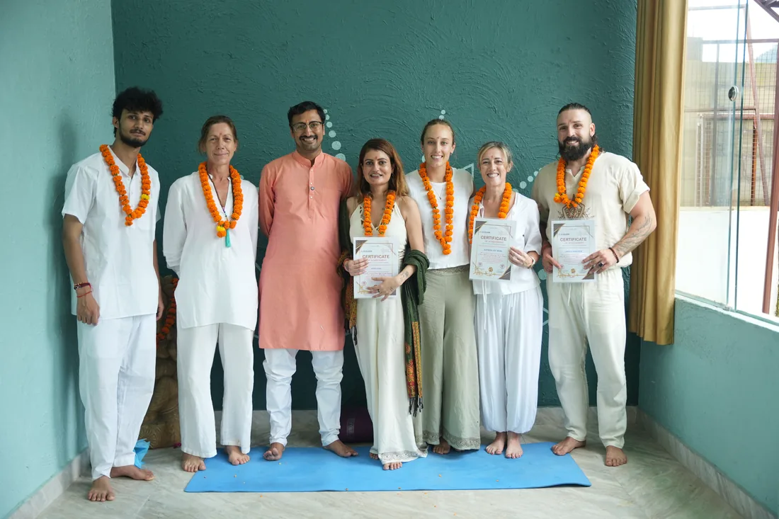 Group of yoga teacher training graduates with garlands and certificates in Rishikesh training hall
